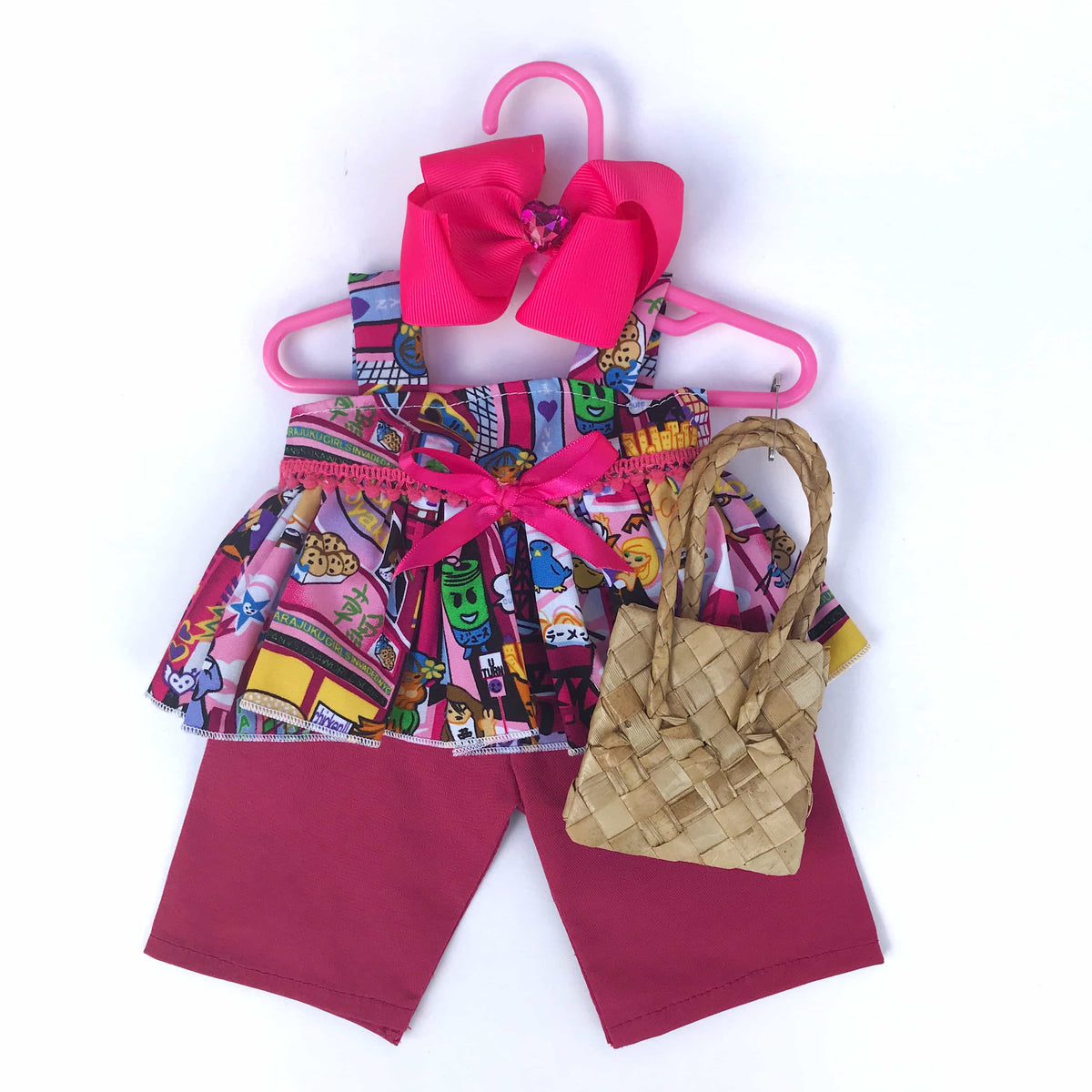 Pink Japanese anime cartoon print two piece outfit for 18 inch American Girl Doll on a hanger  with a natural woven handbag accessory