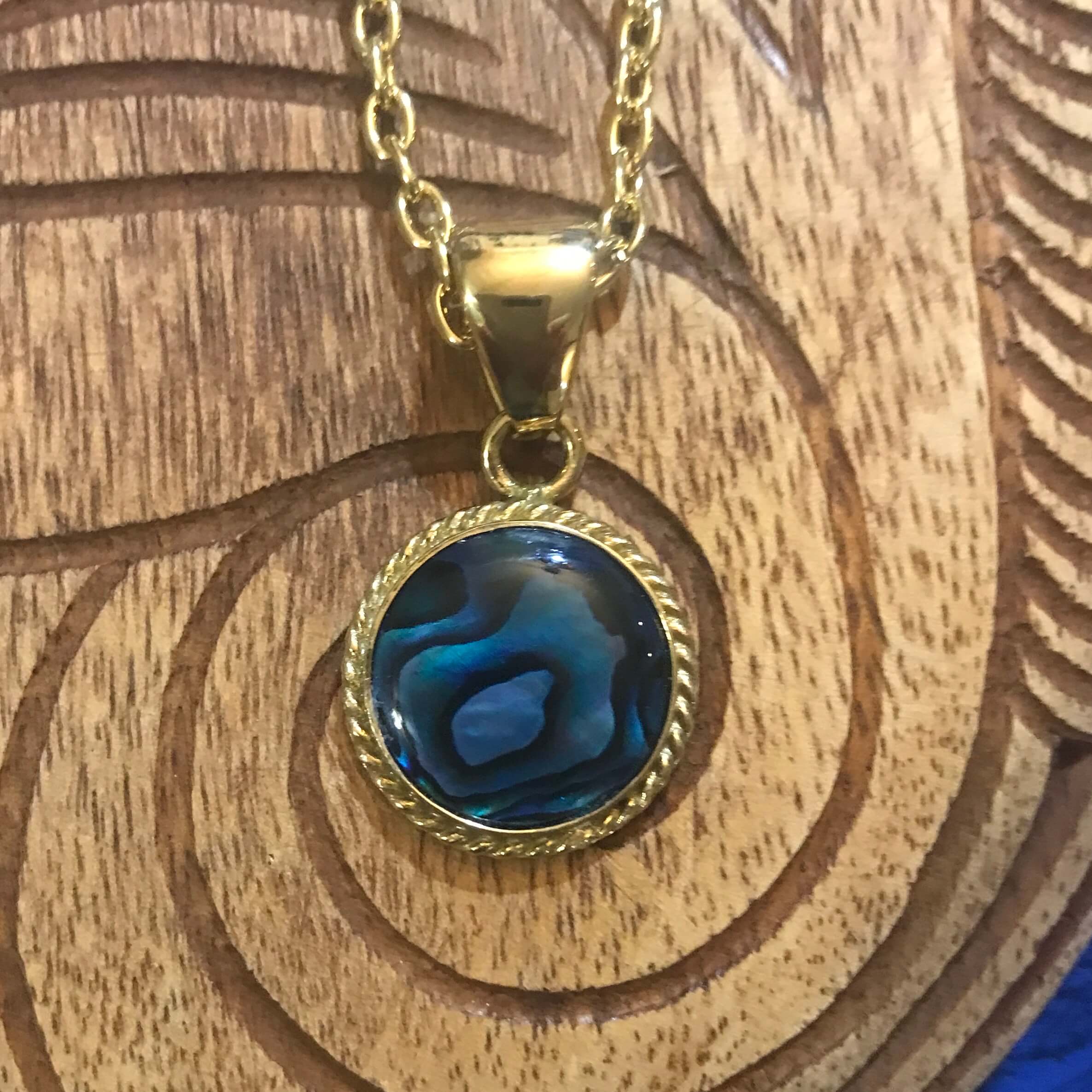 Close up view of a round blue abalone pendant with alchemia gold rope trim around the shell