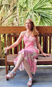 Woman sitting down wearing a beautiful pink Hawaiian halter dress with orchids | Aloha Products USA
