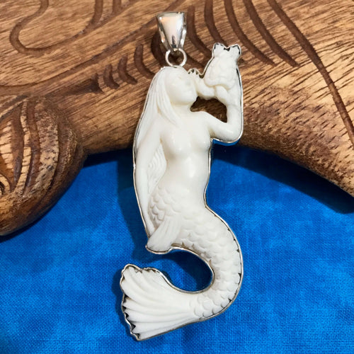 Close up view showing details of a hand carved bone mermaid holding a turtle pendant with stirling silver setting