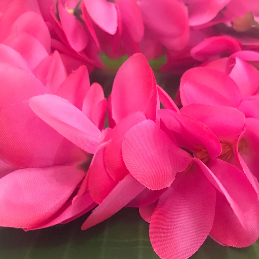 Close up view of a hot pink Hawaiian head lei with plumeria flowers