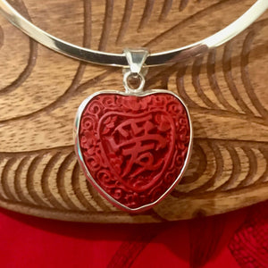 Close up view of a red cinnibar heart shaped pendant necklace with Chinese characters carved into design with a stirling silver setting | Aloha Products USA